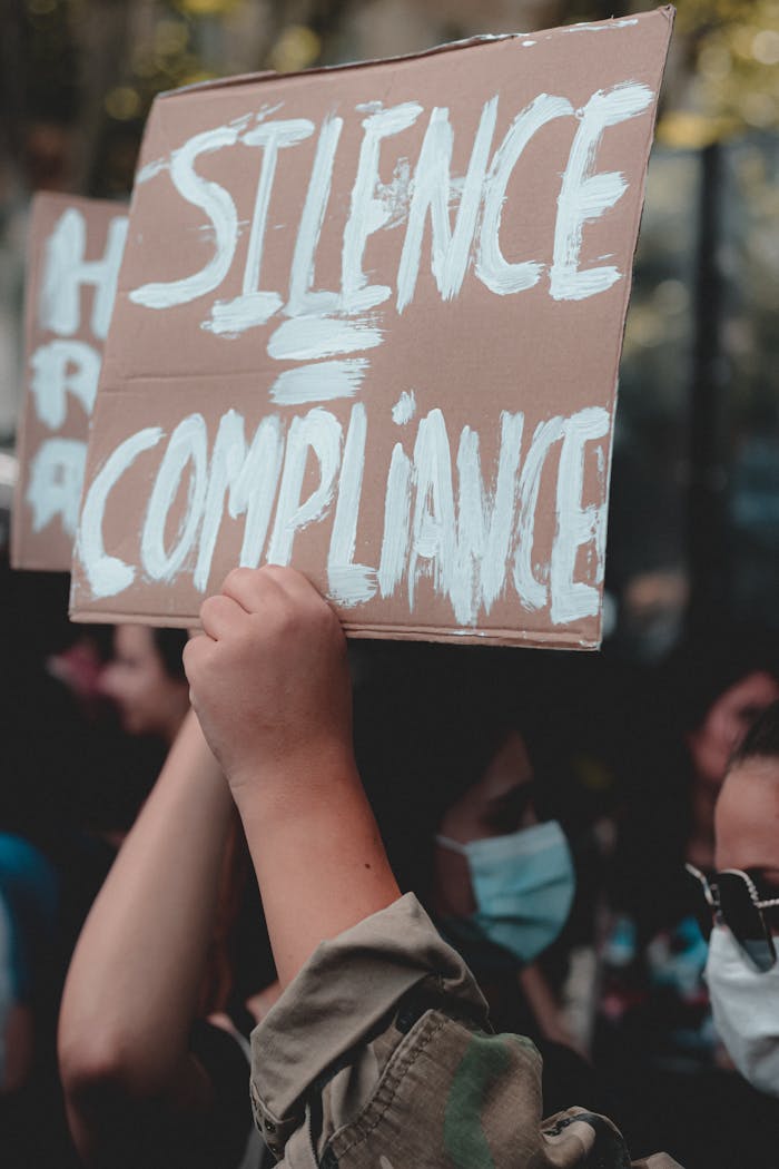 A protest scene highlighting a sign that reads 'Silence = Compliance,' emphasizing social justice and activism.